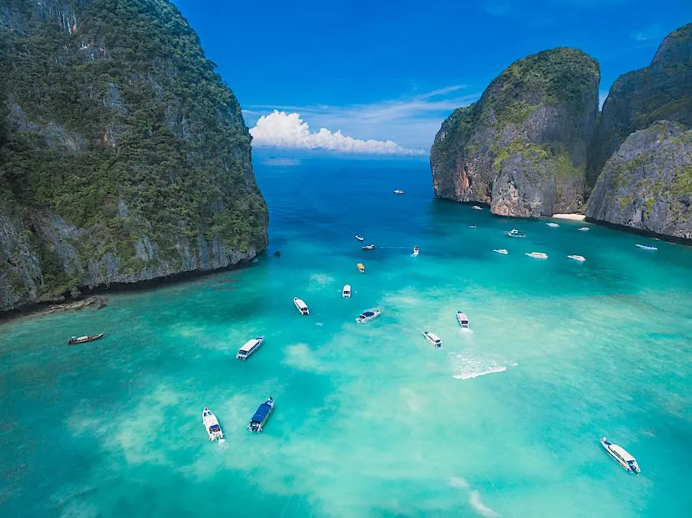 Aerial view of Ko Phi Phi Islands, turquoise-blue water, and longtail boats anchored for snorkeling and swimming.